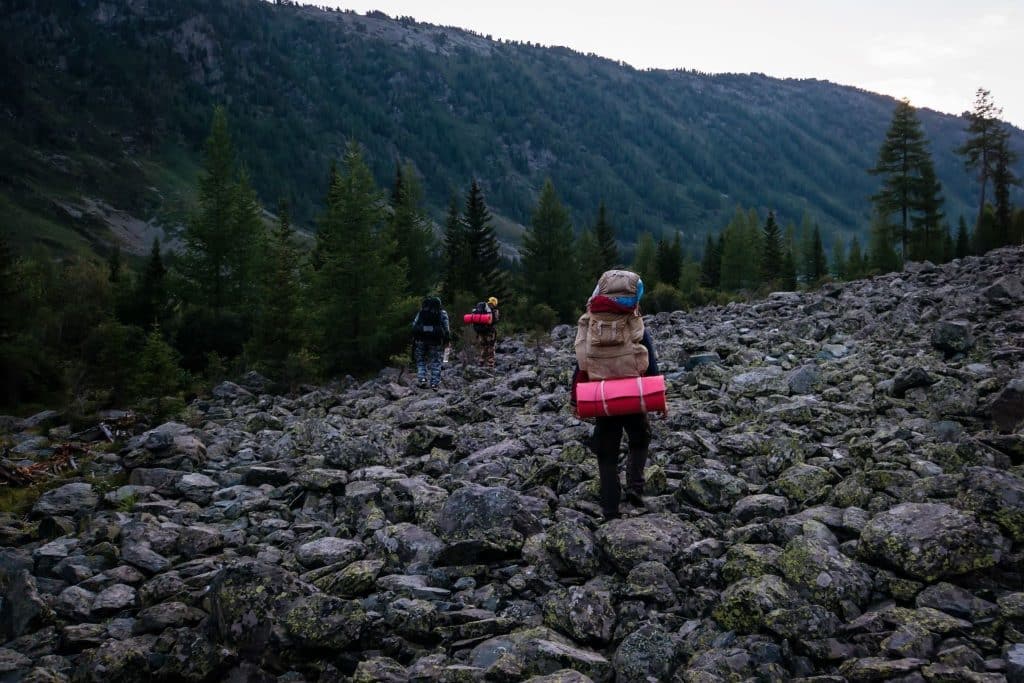 Family hiking across a rocky boulder field with mountains behind.
